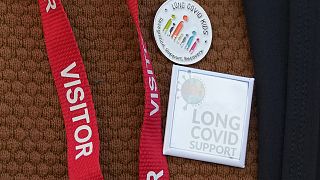 COVID campaigners and families of those who died during the pandemic wear badges in support of children with long covid as they protest outside the COVID Inquiry in London.