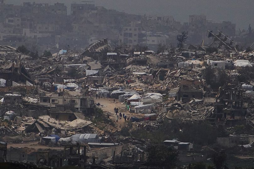 People walking surrounded by buildings destroyed during the Israeli air and ground offensive in Gaza, 20 March, 2025