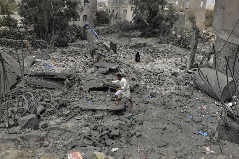 يمني يسير فوق أنقاض مبنى مدمّر جراء غارات جوية أمريكية على صنعاء، اليمن، الإثنين 24 آذار/مارس 2025.
