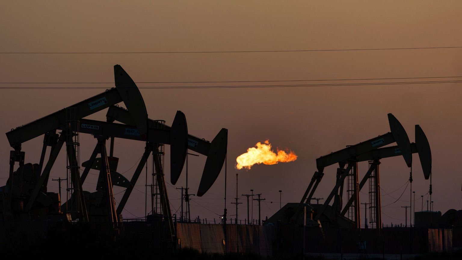 A flare burns off methane and other hydrocarbons as oil pumpjacks operate in the Permian Basin in Midland, Texas, 2021.