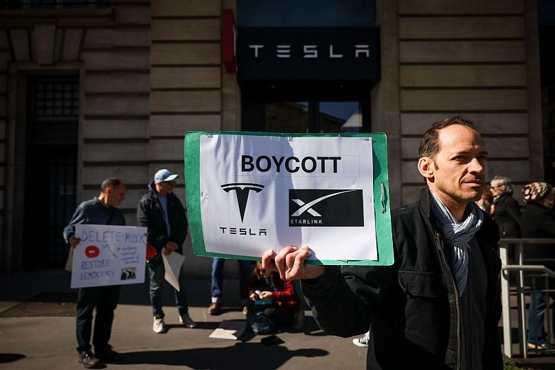 Protestujący trzyma transparent, biorąc udział w Światowym Dniu Akcji Tesla Takedown w pobliżu salonu Tesli w Paryżu, 29 marca 2025 r.