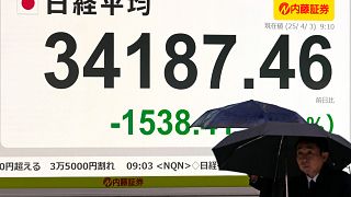 Un grupo de personas pasa por delante de una pizarra electrónica que muestra las pérdidas iniciales del índice japonés Nikkei 225 en una empresa de valores el jueves 3 de abril de 2025 en Tokio.