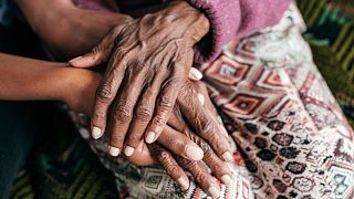 An elderly woman and a younger woman hold hands.