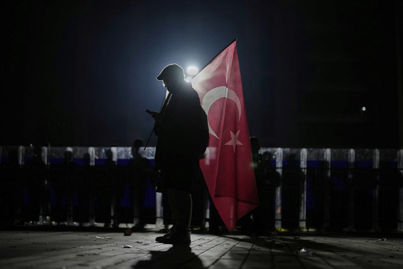 Un manifestante con una bandiera turca davanti alla polizia durante una protesta contro l'arresto del sindaco di Istanbul Ekrem Imamoglu, Istanbul, Turchia, 23 marzo 2025