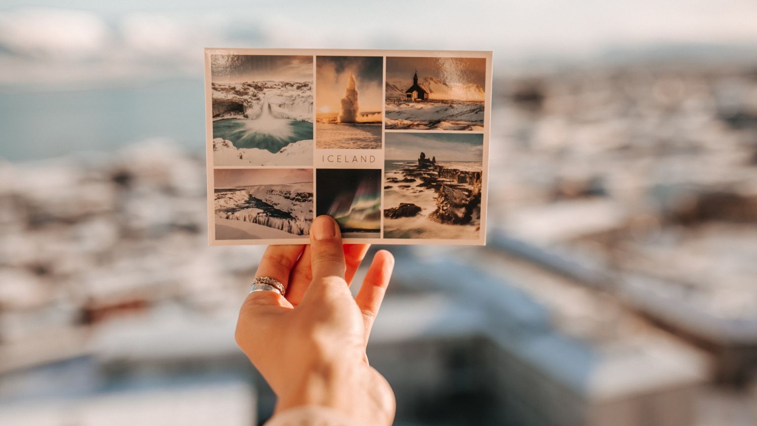 A hand holds a postcard with images of Iceland.