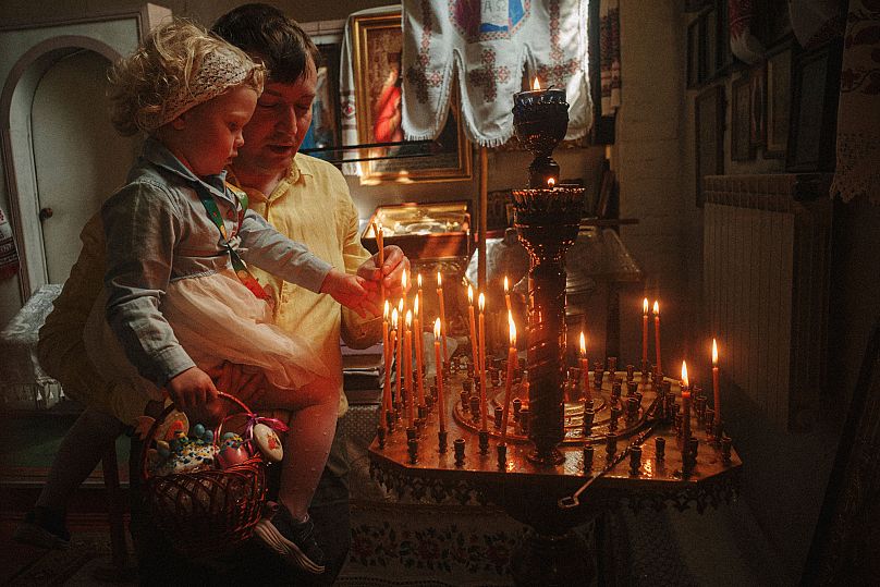 Un père aide sa fille à allumer une bougie lors de la célébration de la Pâque orthodoxe à l'église Saint-Jean Théologien de Kharkiv, en Ukraine, le dimanche 20 avril 2025