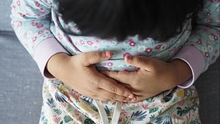 A young child rubs their stomach.