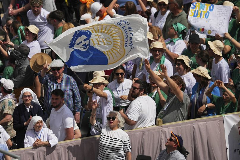 Un homme brandit un drapeau représentant Carlo Acutis, lors d'une messe présidée par le cardinal Pietro Parolin,  sur la place Saint-Pierre, au Vatican, dimanche 27 avril 2025