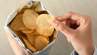 A person pulls a potato chip out of the bag.