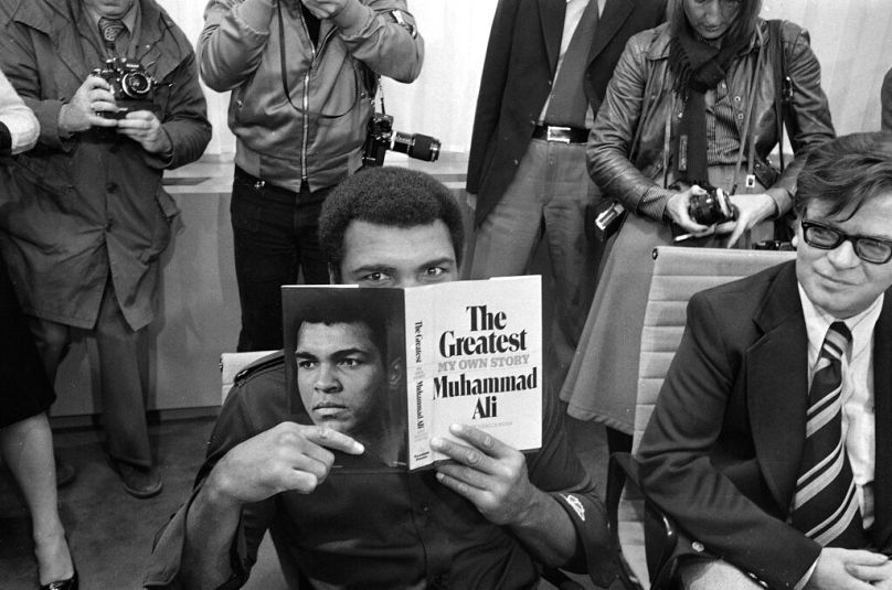 محمد علي يتصفح نسخة من كتابه "الأعظم" في قاعة كبار الشخصيات بمطار فرانكفورت، 10 أكتوبر 1975، خلال مشاركته في معرض فرانكفورت الدولي للكتاب.