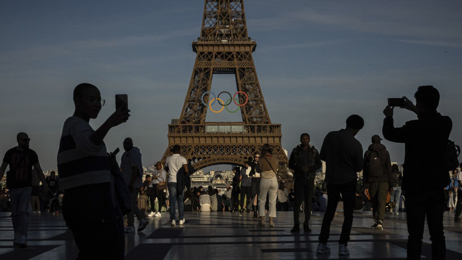 DOSSIER : DOSSIER - Des personnes utilisent leur smartphone près des anneaux olympiques affichés sur la Tour Eiffel à Paris, le 7 juin 2024.
