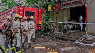 Firefighters stand as policemen guard the entrance of a hotel building which caught fire on Tuesday resulting in several deaths, in Kolkata, India, Wednesday, April 30, 2025.