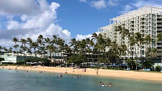 People are seen on the beach and in the water in front of the Kahala Hotel & Resort in Honolulu.