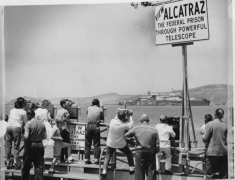 Varias personas observan la Prisión Federal de Alcatraz a través de un telescopio tras una fuga. Foto tomada el 16/06/1962.