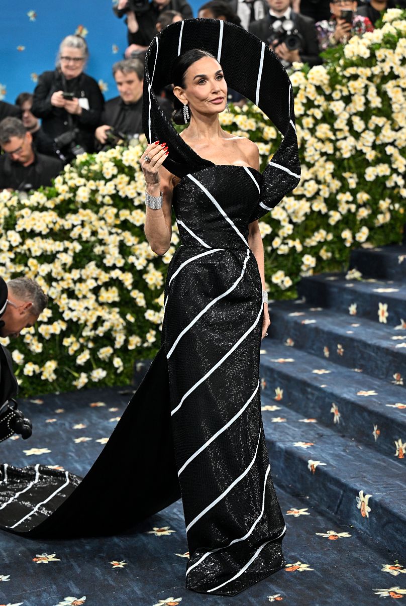 Substance yıldızı Demi Moore, siyah-beyaz omuzları açık bir elbise ve gösterişli hilal şeklindeki başlığıyla göz kamaştırdı.