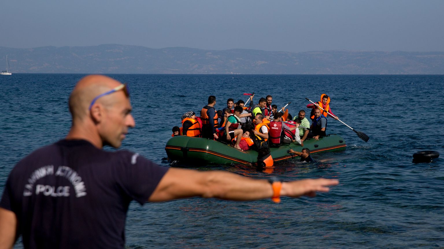 A Greek policeman gives instructions as migrants whose boat stalled at sea while crossing from Turkey to Greece approach the shore of Lesbos, 20 September, 2015
