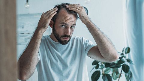 A balding man checks his hairline.
