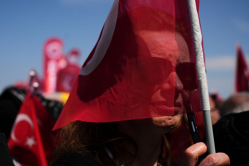 A woman holds a Turkish flag as she listens to speeches during a rally in Istanbul, March 2025