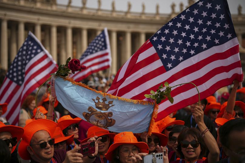 Faithful wave flags from the United States as they wait for Pope Leo XIV to appear at the central balcony of St. Peter's Basilica for his first Sunday blessing.