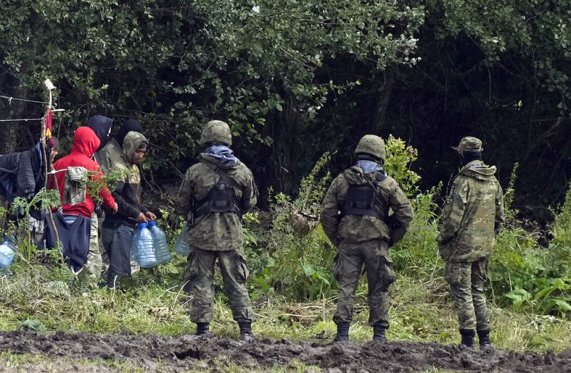 Migranci utknęli wzdłuż granicy polsko-białoruskiej, niosąc plastikowe butelki z wodą, otoczeni przez polskie siły w Usnarzu Górnym w Polsce, w środę 1 września 2021 r.