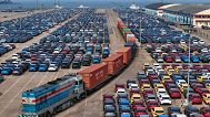 A cargo train moves past new cars waiting for shipment in a port, in Yantai in east China's Shandong province, 7 May 2025