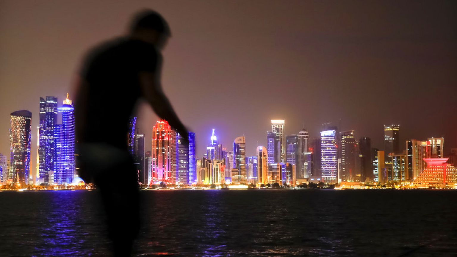 In this Friday, Nov. 2 2018. picture a man walks backdropped by the skyline of Doha, Qatar.