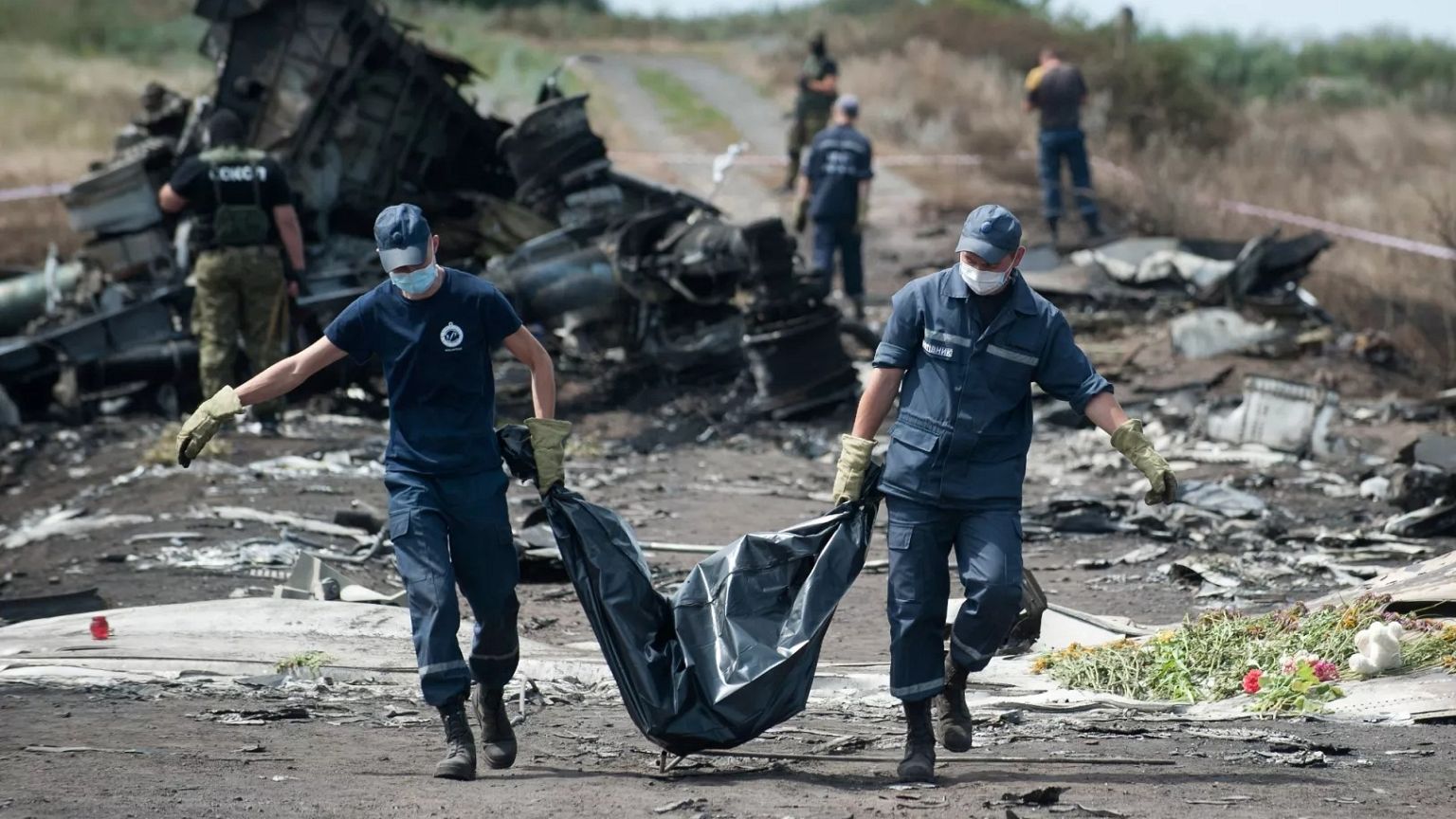 Des secouristes ukrainiens transportent le corps d'une victime dans un sac mortuaire alors que des combattants pro-russes montent la garde sur le site du crash du vol MH17 de la Malaysia Airlines, le 20 juillet 2014.