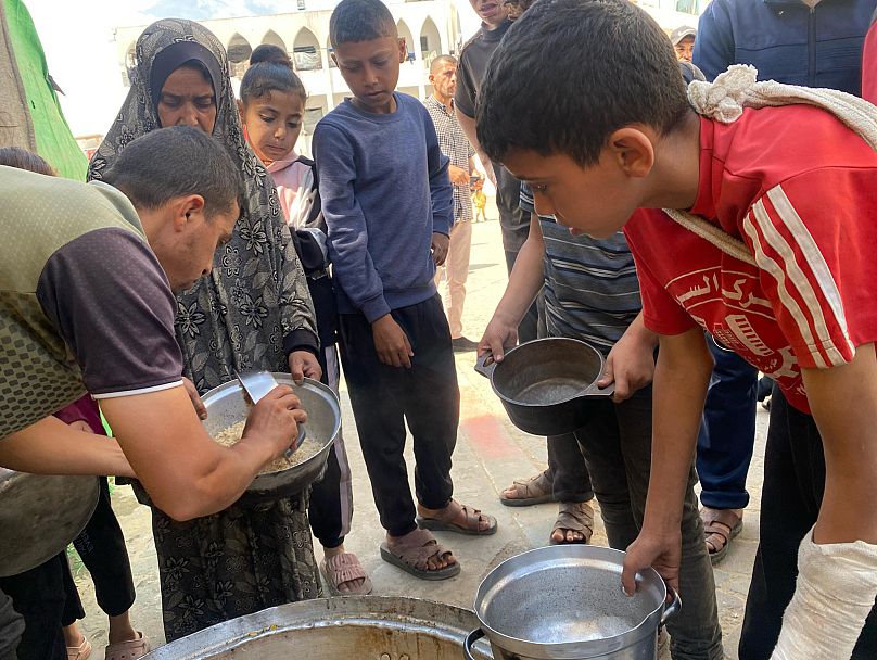 أطفال ينتظرون توزيع وجبة ساخنة في دير البلح بقطاع غزة، 14 مايو أيار 2025
