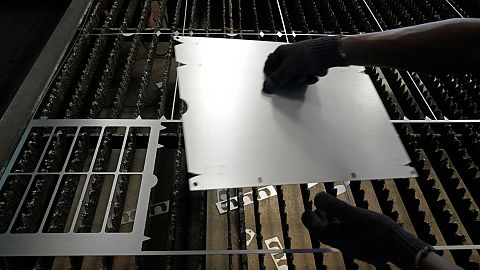 A worker lifts a steel sheet after cutting it in a specific design at a factory in a suburb of Bengaluru, India.