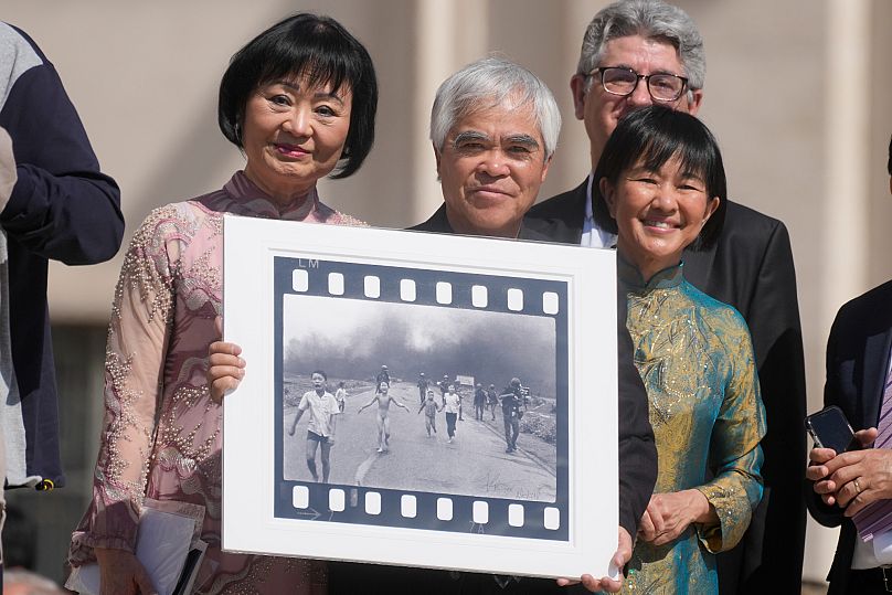Nick Ut, center, holds his Pulitzer-winning "Napalm Girl" photo alongside Kim Phuc, left, as they await a meeting with Pope Francis at the Vatican, 11 May 2022.