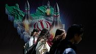 Iranian women walk past a banner showing missiles being launched from an Iranian map in Tehran, 19 April, 2024