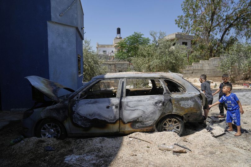أطفال فلسطينيون يلعبون قرب مركبة عائلتهم التي أُحرقت خلال هجوم ليلي نفذه مستوطنون إسرائيليون، في بلدة بروقين، الجمعة 23 أيار/مايو 2025.