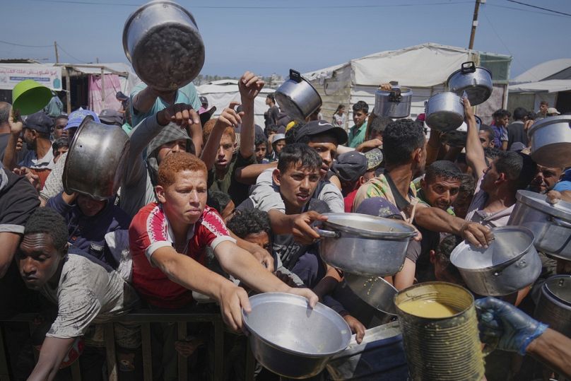 فلسطينيون يحاولون الحصول على وجبات طعام بمنطقة المواصي في خان يونس، جنوب قطاع غزة، الجمعة 23 أيار/مايو 2025 