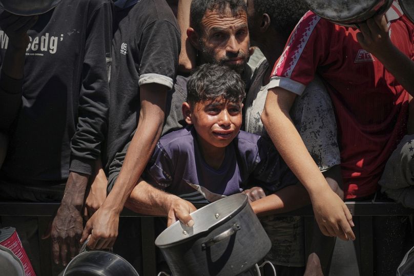 فلسطينيون يحاولون الحصول على وجبات من مطبخ مجتمعي في منطقة المواصي بخان يونس، غزة – الجمعة 23 أيار/مايو 2025.