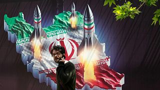 A passerby walks past a banner showing missiles being launched from Iranian map in northern Tehran, 19 April, 2024
