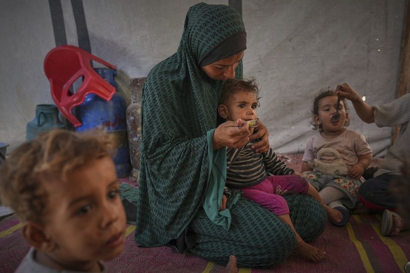 Una mujer palestina alimenta a sus hijos en una tienda de campaña que alberga a una familia desplazada en el centro de la ciudad de Gaza, el sábado 24 de mayo de 2025.