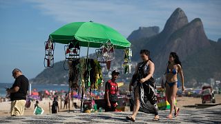 Beachgoers walk past a vendor's stand of beachwear on Ipanema Beach in Rio de Janeiro.