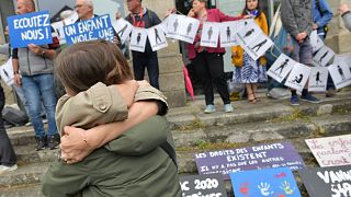 People hug as demonstrators hold a banner representing anonymous victims during the trial of Joel Le Scouarnec in Vannes, 28 May, 2025 