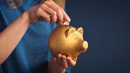 A woman putting a coin into a piggy bank. 