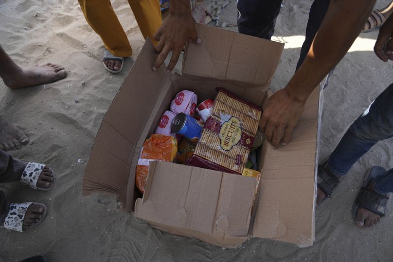 Varios palestinos abren una caja que contiene alimentos y paquetes de ayuda humanitaria entregados por la Fundación Humanitaria de Gaza, una organización respaldada por EE.UU.