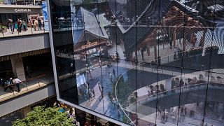 People tour by a projector screen promoting a newly opened outdoor Hutong style shopping mall, in Beijing, Monday, May 26, 2025.