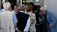 A pensioner waits to enter a bank as others stand in a queue to use an ATM of the branch in Athens