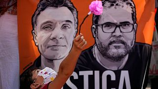A boy plays with a flower in front of a banner with images of British journalist Dom Phillips, left, and Indigenous expert Bruno Pereira, June 2022.