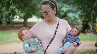 Ana Paula Vilela holds her dolls during a group gathering to bond and show off their hyper-realistic reborn baby dolls, in a park in Sao Paulo, Saturday, May 24, 2025. 
