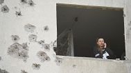A woman looks though the window of her damaged apartment following a Russian strike in Kharkiv, 18 April, 2025