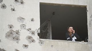 A woman looks though the window of her damaged apartment following a Russian strike in Kharkiv, 18 April, 2025