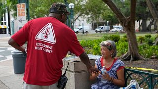 Ricky Leath, an outreach specialist with the City of Miami, talks with Bei Zhao, right, as he works with the Miami-Dade County Homeless Trust to distribute bottles of water