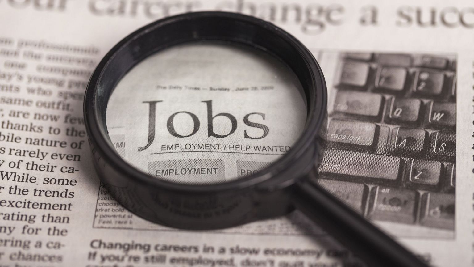 A magnifying glass on a newspaper enlarging the word "jobs".