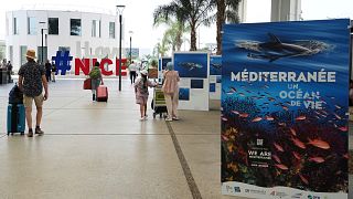 People leave the airport near signs ahead of the upcoming UN Ocean Conference in Nice.