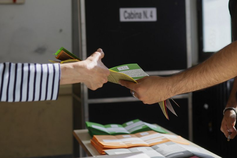 Des bulletins de vote sont remis à un citoyen, à gauche, pour voter sur des référendums sur la citoyenneté et la protection de l'emploi, dans un bureau de vote à Rome.